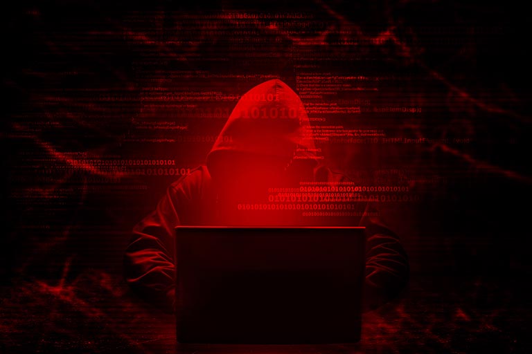 Abstract hacker image featuring a hooded figure at a laptop