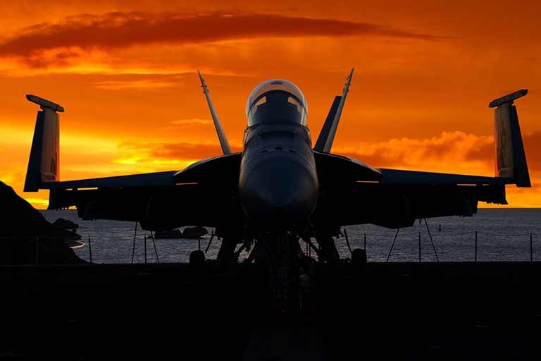 A military jet on the deck of an aircraft carrier with a dramatic sunset